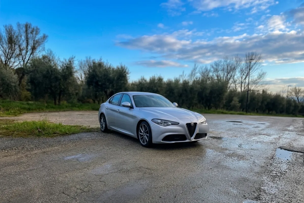 Alfa Romeo Giulia grigia ferma su un piazzale bagnato, tra gli ulivi