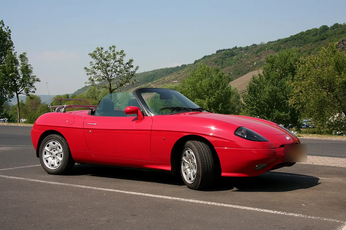 Fiat Barchetta rossa scoperta, ferma in un piazzale con le colline sullo sfondo