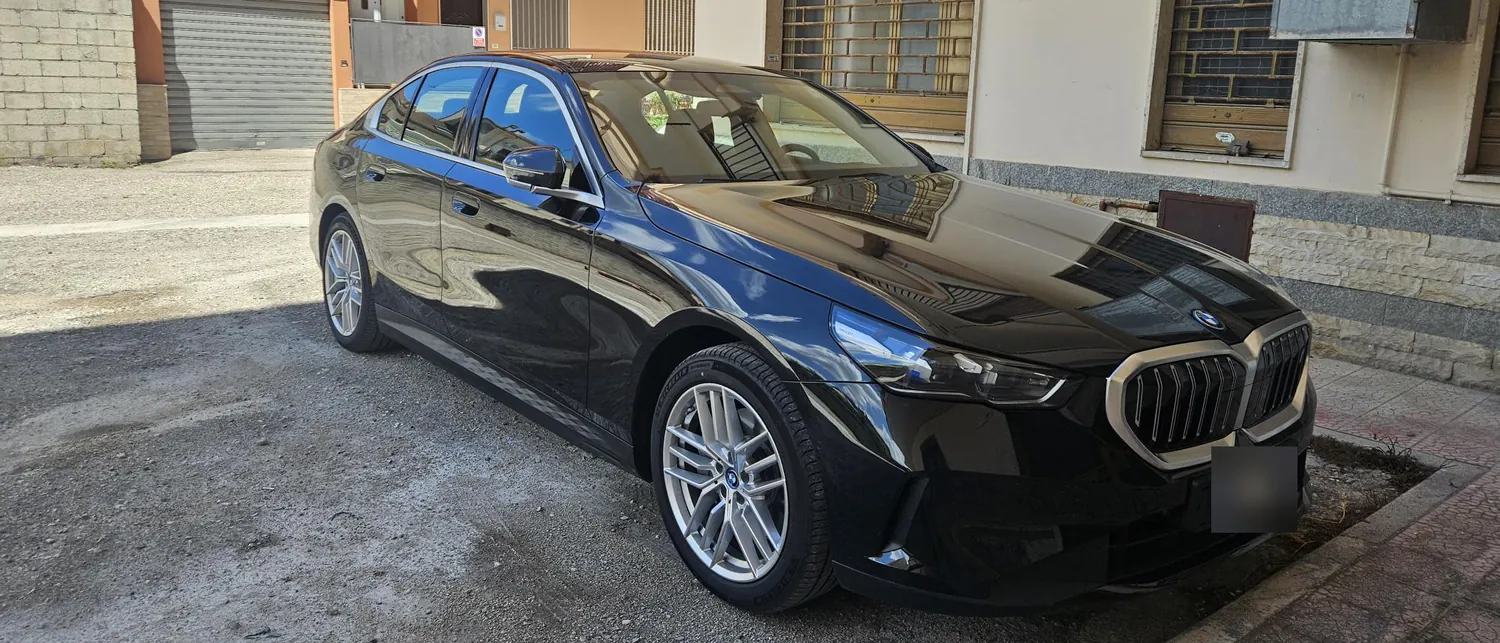 La BMW i5 nera vista di tre quarti anteriore, parcheggiata in una strada di paese