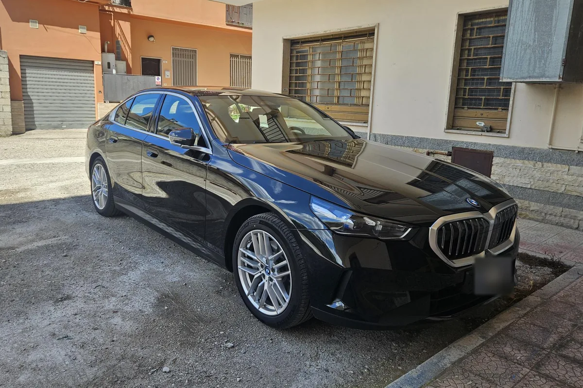 La BMW i5 nera vista di tre quarti anteriore, parcheggiata in una strada di paese