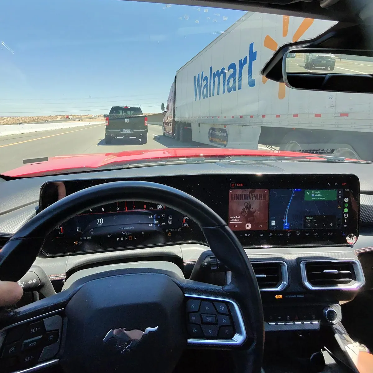 Vista dal posto di guida in autostrada, dietro un camion: cruscotto digitale a 70 miglia orarie e schermo dell'infotainment