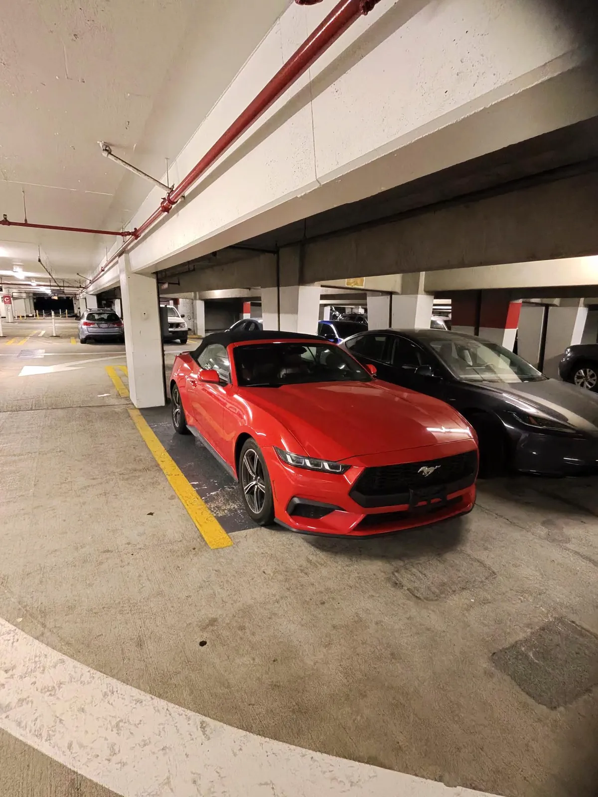 La Mustang con la capote chiusa in un parcheggio sotterraneo, accanto a un'auto scura