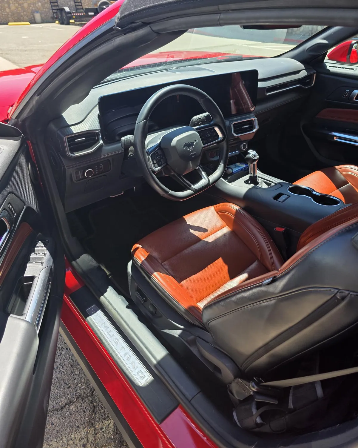 Il posto di guida della Mustang visto dalla portiera aperta: sedili in pelle arancione, volante e schermi digitali