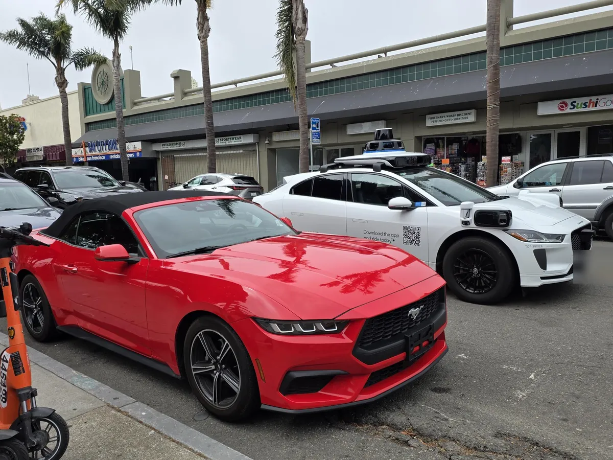 La Mustang rossa parcheggiata in una via di San Francisco, accanto a un Jaguar bianco di Waymo con i sensori sul tetto
